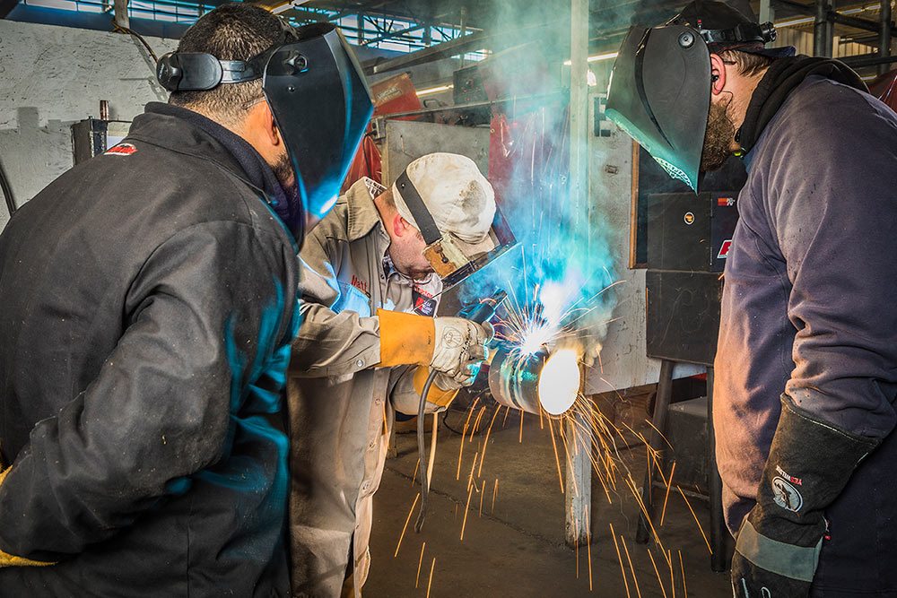 Group of students watching instructor weld a pipe